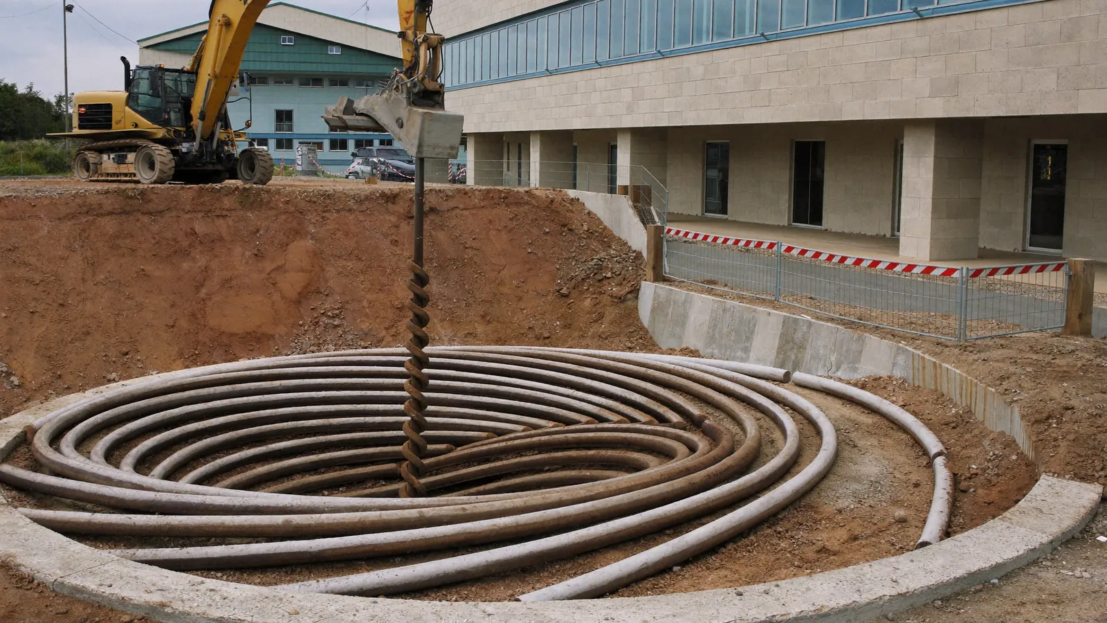 Helical pier being driven by hydraulic machine alongside the footing of a low-rise commercial masonry building in an Oklahoma City metro business park