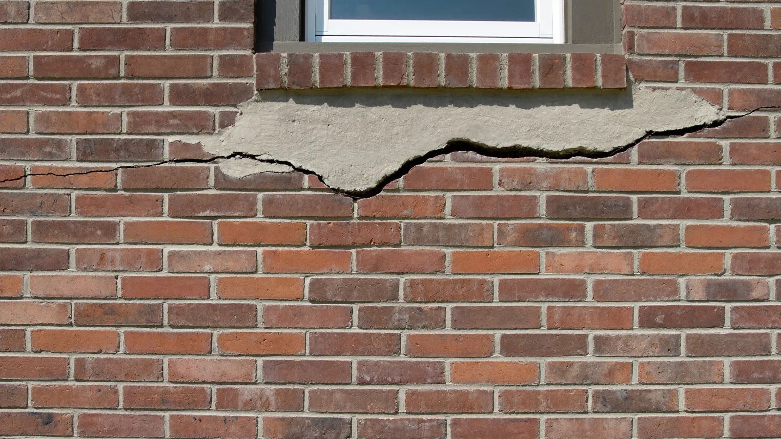 Stair-step crack running diagonally through the mortar joints of a red brick veneer wall on an Oklahoma house, widening toward the corner